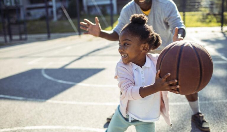 Close up of a grandfather taking his granddaughter to play some basketball in the park