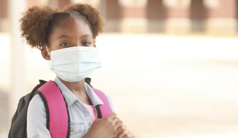 Back to school. African descent girl on school campus. She wears a mask for COVID-19, Coronavirus protection.