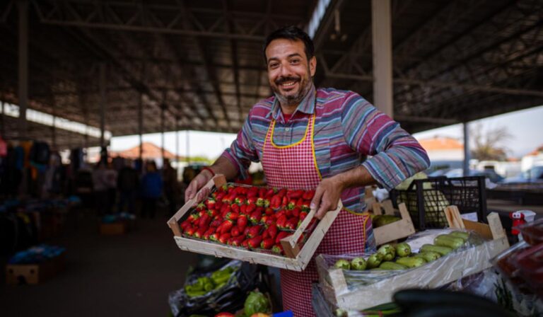Portrait of male farmer holding a crate full of strawberries at the marketplace.