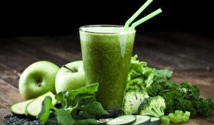 Glass of fresh green vegetable juice with two drinking straws on rustic wood table. The glass is surrounded by green vegetables like spinach, lettuce, broccoli, celery, green apples, parsley and cucumber. This is a drink used for detox diet. Predominant colors are green and brown.