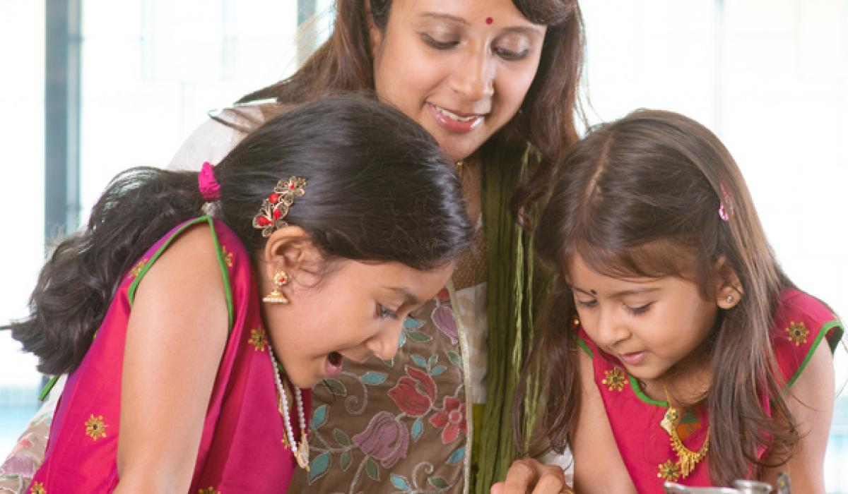 Asian family cooking food together in kitchen. Indian mother and children preparing meal at home. Traditional India people with sari clothing.