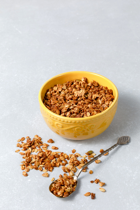 Homemade oatmeal granola bowl with spoon on light grey background.