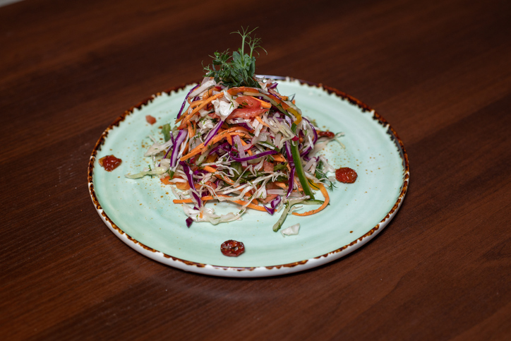 A plate of salad with carrots and tomatoes on a wooden table. The salad is colorful and appetizing