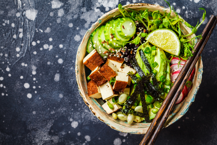 Poke bowl with avocado, black rice, smoked tofu, beans, vegetables, sprouts, dark background.