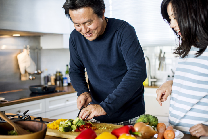 A father and his daughter chopping vegetables in the kitchen.