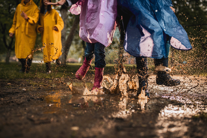 Youth wearing multicolored raincoats playing in rain.