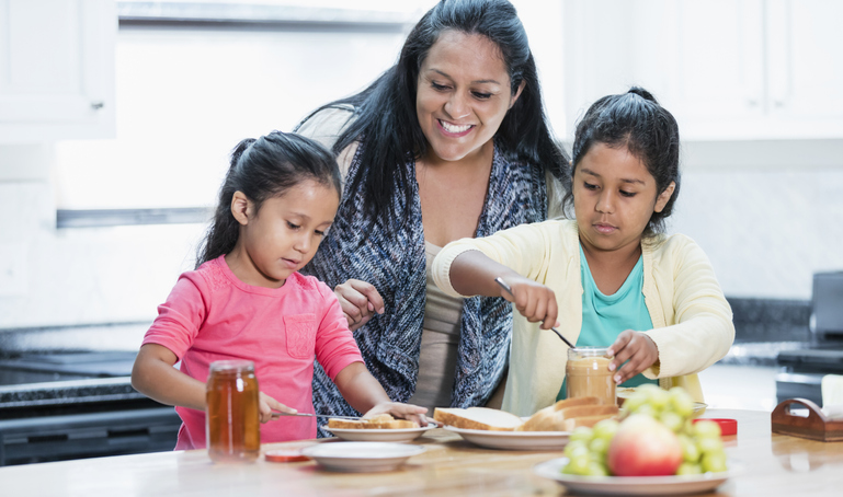 Mother with two children preparing a snack together in a kitchen.