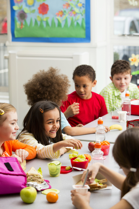 Children eating lunch at a table in a school cafeteria.