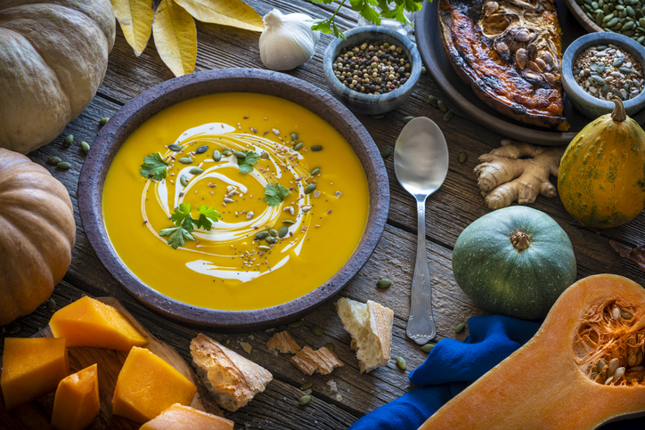 Squash, carrots, kale in a basket on wooden background.