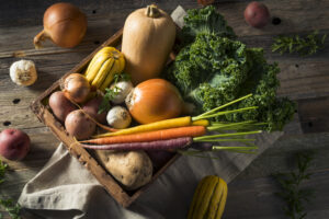 Squash, carrots, kale in a basket on wooden background.