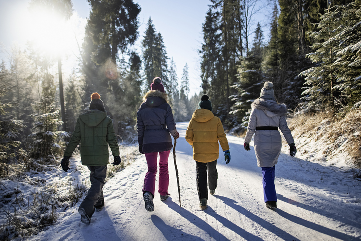 Family is hiking in winter forest. Kids with mother are walking on snow covered road, talking and enjoying the winter.