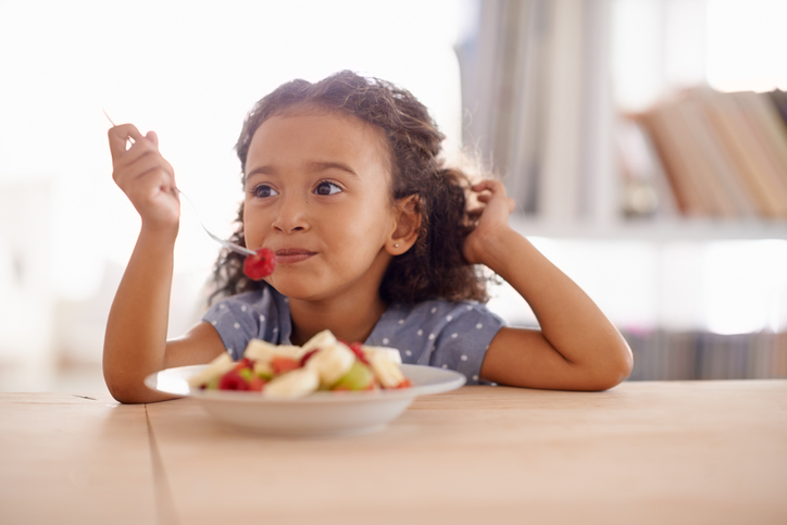 Shot of a cute little girl eating fruit salad at a table