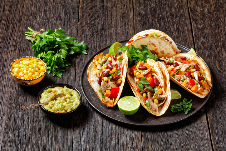 tacos of flour tortilla shells filling with grilled chicken meat, corn, roasted sweet potatoes cubes, red pepper and parsley served on a black plate