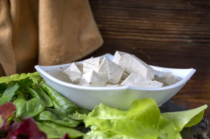 Fresh vegan product - tofu. Soy gray tofu on a plate marinated with spices and salad leaves