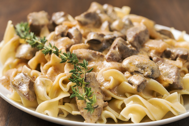 A plate full of creamy beef stroganoff made with egg noodles, mushrooms and garnished with fresh rosemary.