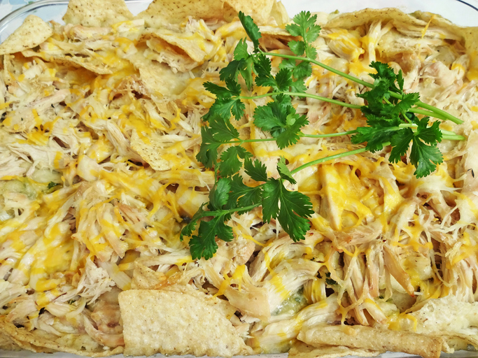 Photo of Mexican food casserole dish called Chilaquiles garnished with cilantro. This is made from tomatillo salsa, tortilla chips, shredded chicken breast and Mexican cheese. This dish can be served with sour cream and guacamole.