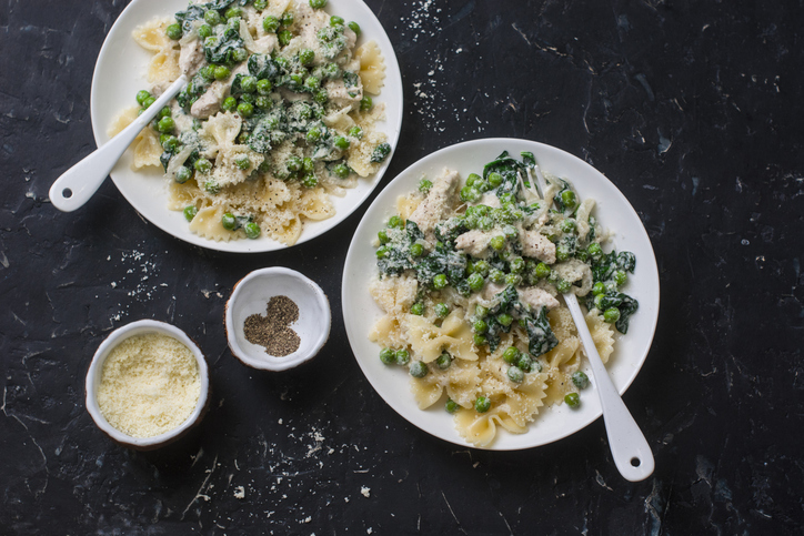 Creamy chicken, green peas, spinach farfalle pasta on a dark background, top view. Mediterranean style healthy eating