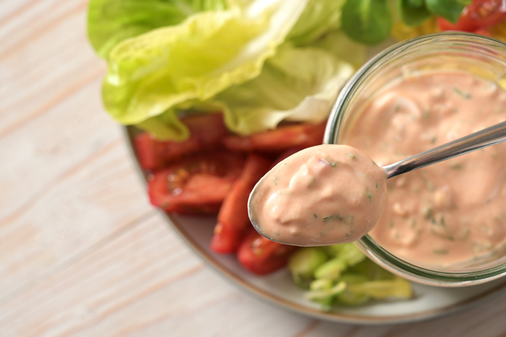 Thousand Island sauce based on skyr on a spoon and in a glass jar over slices of lettuce and tomato salad, healthy raw food meal, selected focus