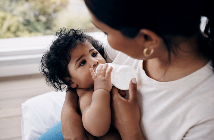 Shot of a woman sitting on the bed at home and feeding her baby daughter with a bottle