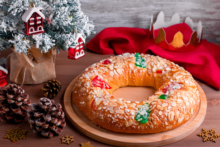 Traditional Epiphany cake Roscon de Reyes with paper crown on wooden table top with small Christmas tree and decoration closeup, top view