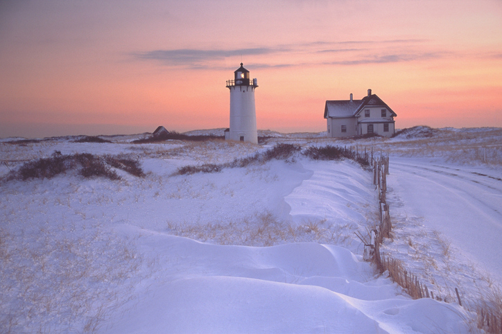 Race Point Lighthouse is located on Cape Cod where it guards the entrance to Provincetown Harbor. Surrounded by wild windswept dunes, it is accessible only by four-wheel-drive vehicle or by foot. Photo taken at sunset surrounded by snow covered dunes. Cape Cod is famous, worldwide, as a coastal vacation destination