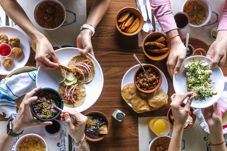 Group of latin Friends eating Mexican Tacos and traditional food, snacks and peoples hands over table, top view. Mexican cuisine Latin America