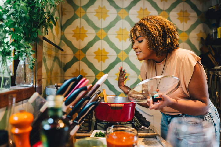 Woman smelling food cooking in a pot on her kitchen stove