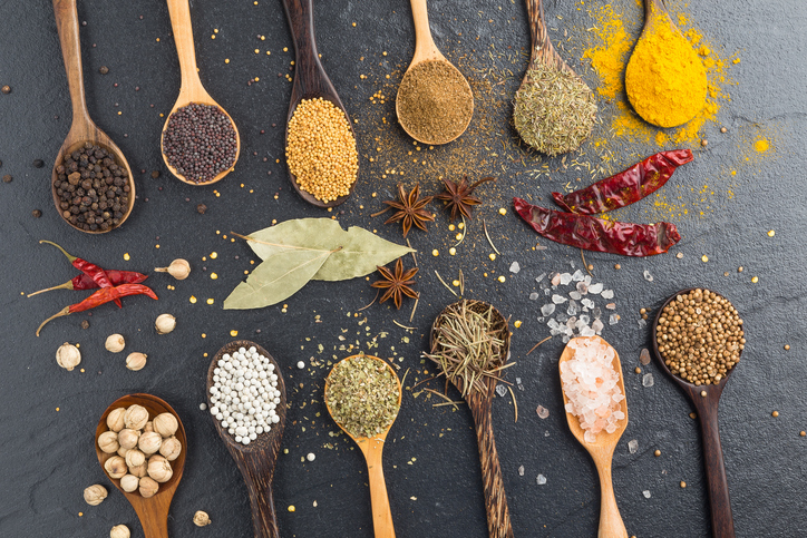 Variety of herbs and spicies ingredients. peppercorn, mustard, oregano, turmeric, paprika, pepper, anise, coriander, rosemary, salt, thyme, bay leaf on black stone background.