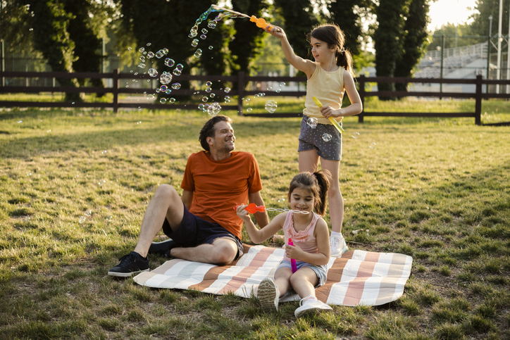 Father enjoying with his two girls at the park, while they're playing with bubbles