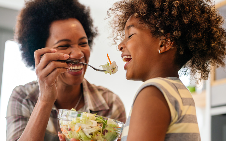 Mother feeding her daughter, both are laughing