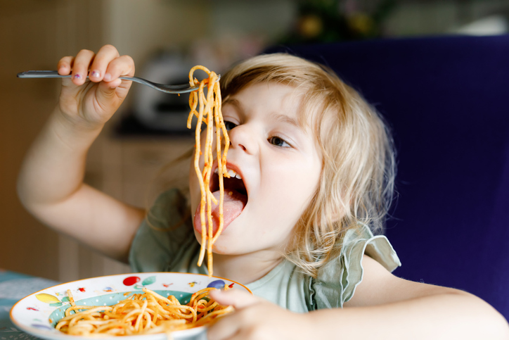 Adorable toddler girl eat pasta spaghetti with tomato bolognese with minced meat. Happy preschool child eating fresh cooked healthy meal with noodles and vegetables at home, indoors