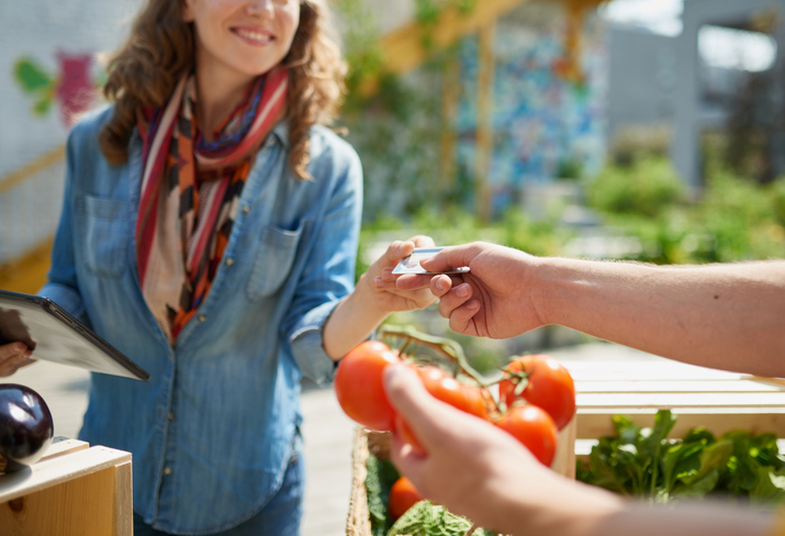 Female gardener selling organic crops and picking up a bountiful basket full of fresh produce