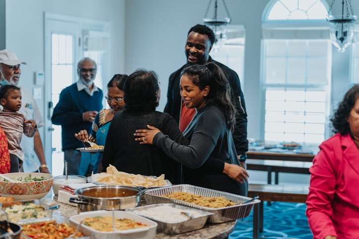 Young Indian woman hugs an elder woman with a hug during a family celebration, while she smiles up at a young man.