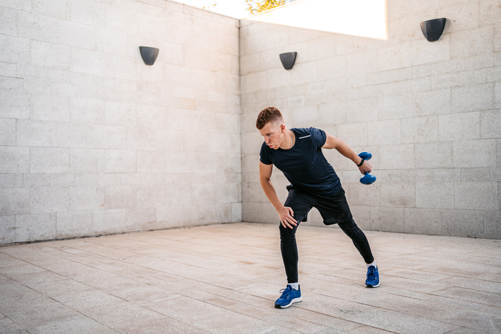 Young Man Doing Single Arm Tricep Kickbacks Outdoors