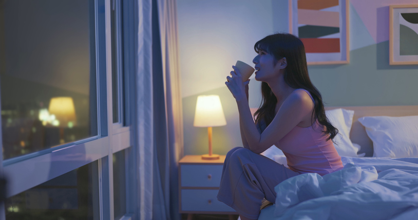 Side view of woman sit aside bed happily herb tea before bedtime which is good for sleeping and life enjoyment