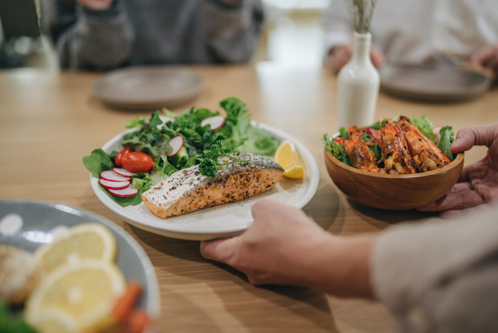 Young family having lunch at home. On the table are seafood,grilled salmon, couscous, grilled shrimp, asparagus with eggs and salad