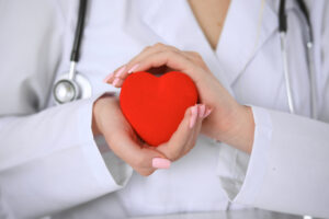 Female doctor with stethoscope holding heart. Patients couple sitting in the background