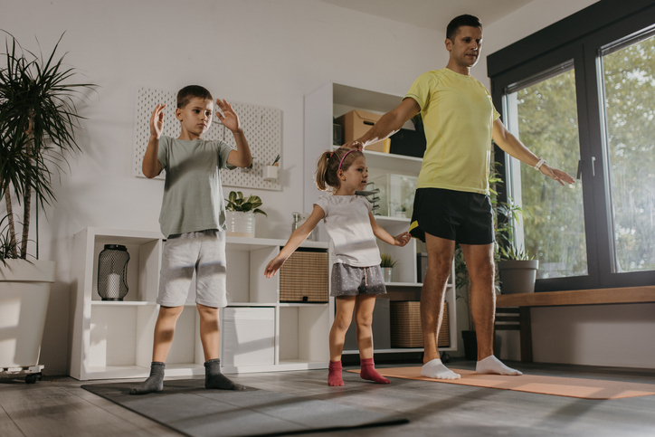 Father with little son and daughter having fun exercising in living room at home together.