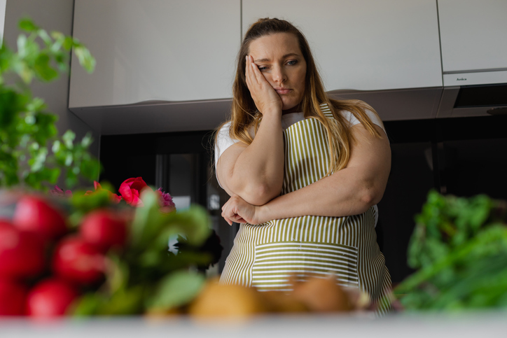 Tired, sad and bored  blond woman holding head in hand, thinking what to cook, have no idea. Looking for recipe